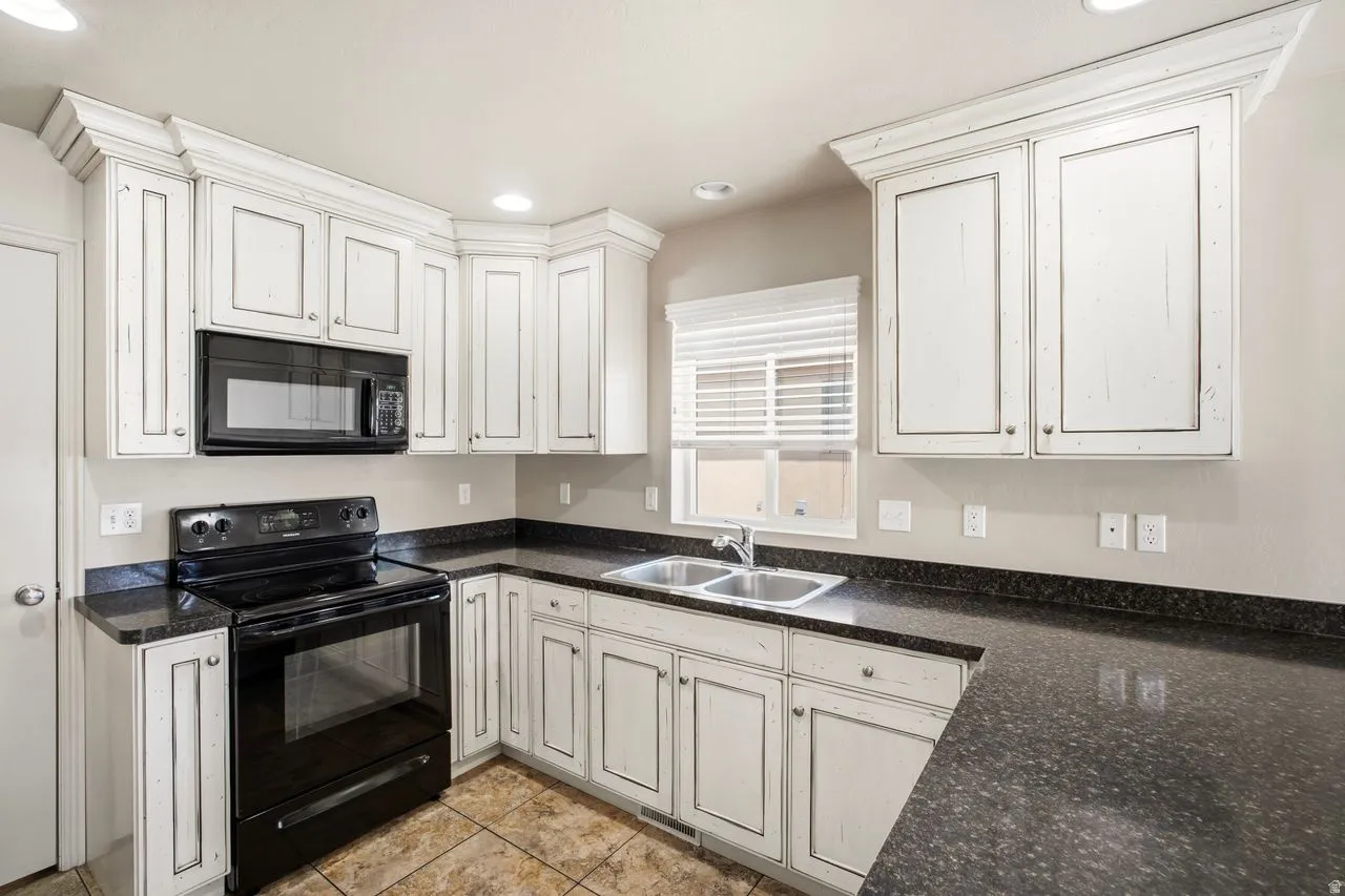Kitchen featuring distressed white cabinetry, dark speckled countertops, and a full suite of black appliances