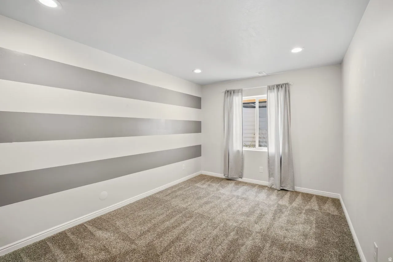 Carpeted room featuring a window with light-filtering curtains, recessed lighting, and a horizontally striped accent wall