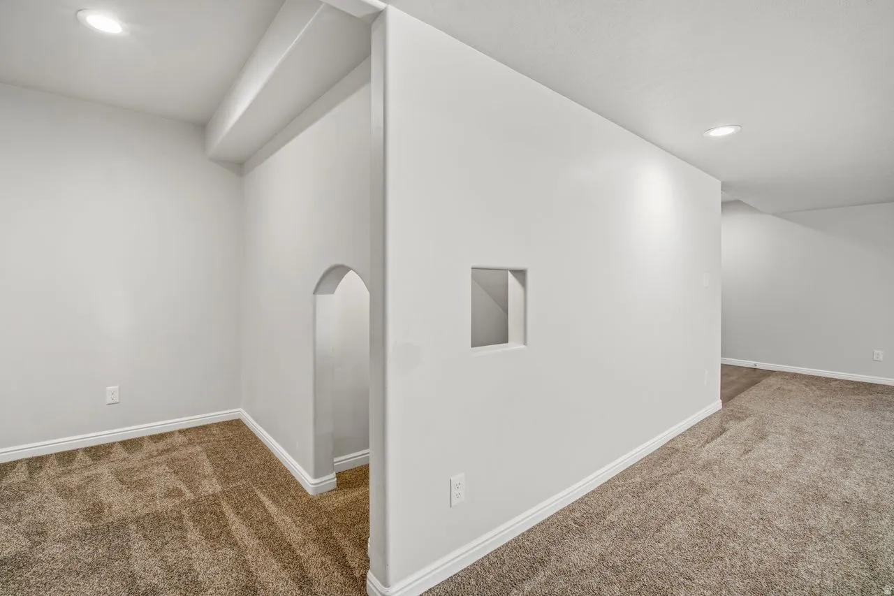Carpeted interior space featuring an arched doorway, recessed lighting, and a wall cutout
