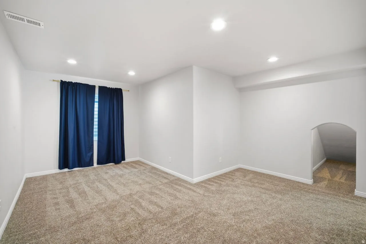 Spacious room featuring neutral carpeting, white walls, recessed ceiling lighting, and a window with dark curtains