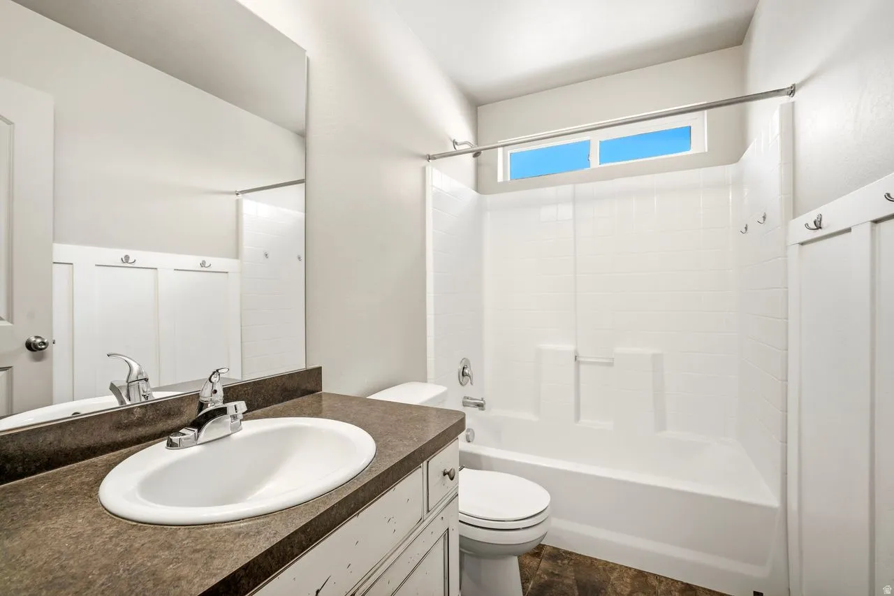 Bathroom featuring a vanity with an integrated sink, a rectangular mirror, a bathtub with a shower, a toilet, and an upper window