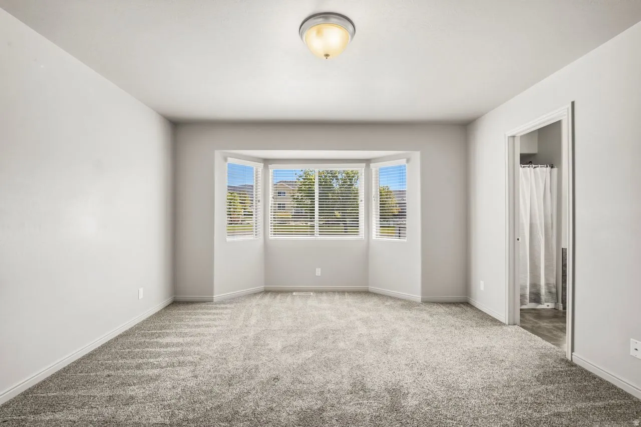 Bright room featuring a three-panel bay window with horizontal blinds, neutral-toned walls, and gray carpet flooring
