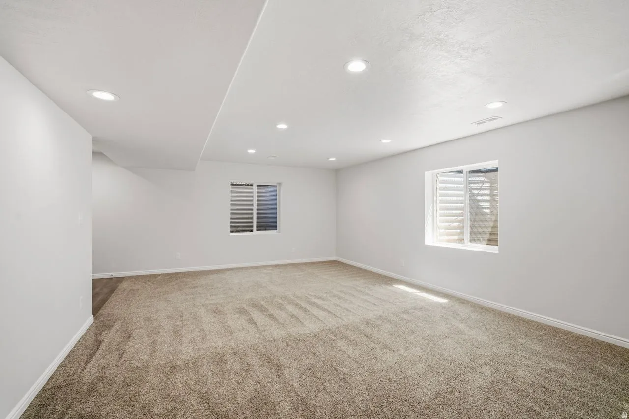 Spacious room featuring neutral carpet flooring, recessed lighting, and two windows with horizontal blinds
