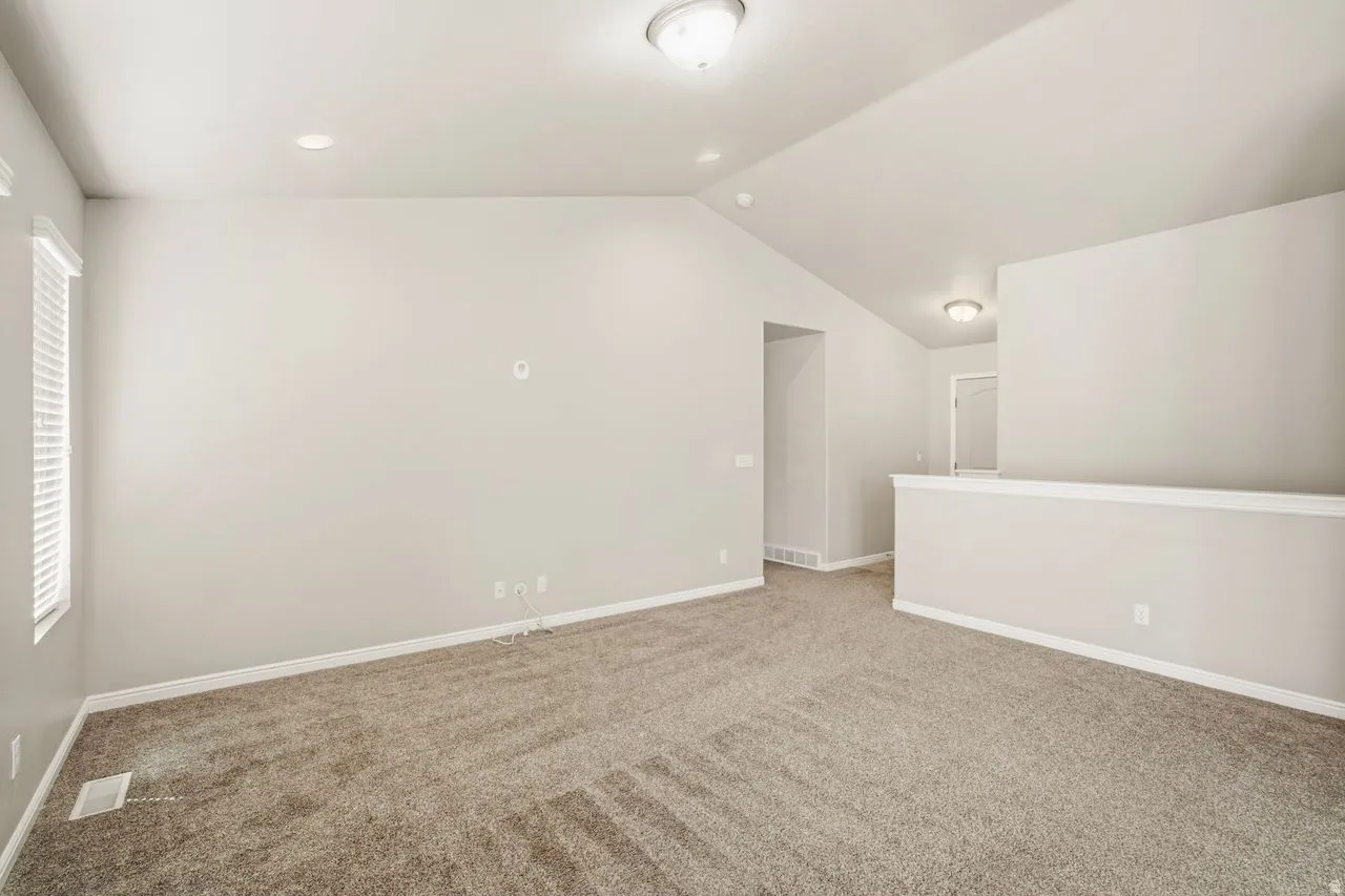 Spacious room featuring vaulted ceilings, neutral-toned walls, and plush patterned carpeting