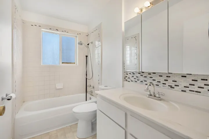 Bathroom featuring a white vanity with an integrated sink, mosaic tile backsplash, and a three-door mirrored medicine cabinet