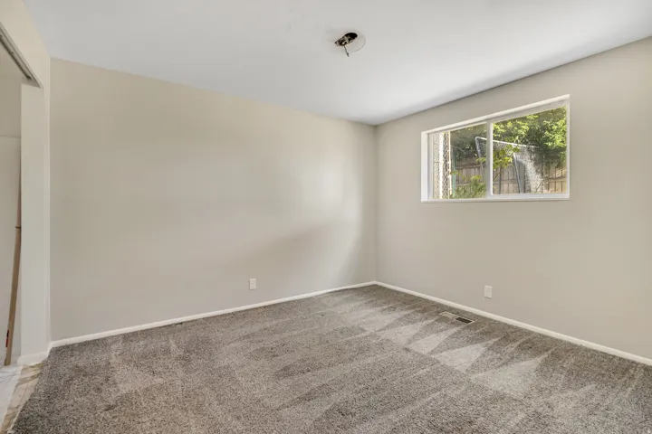 Neutral tone wall paint with white trim, gray patterned carpet, a single window, and a small built-in closet