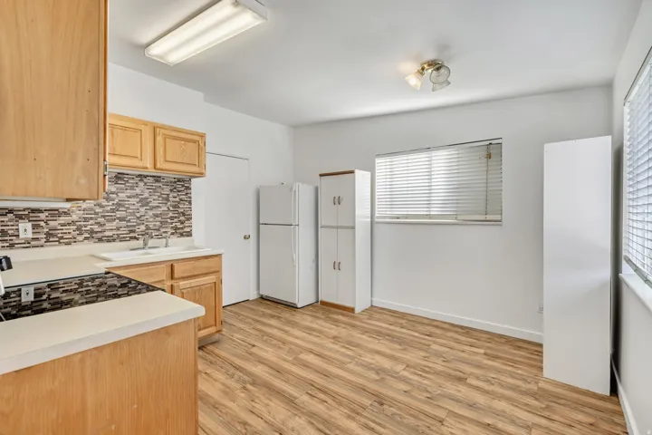 Kitchen featuring wood-finish flooring, light wood cabinetry, white countertops, and a patterned tile backsplash