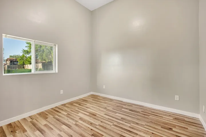 Interior space featuring wood-finish flooring, light neutral wall tones, high ceilings, and a large window