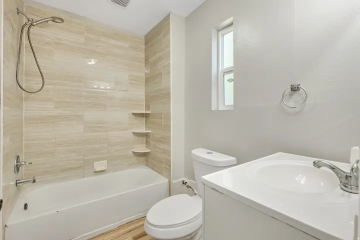 Bathroom featuring a white bathtub, ceramic tile shower surround with integrated shelving, white vanity with integrated sink, and wood-finish flooring