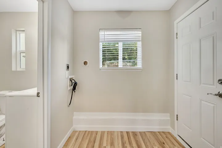 Utility room featuring wood-finish flooring, a functional window with blinds, and a paneled entry door