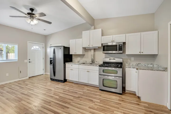 Kitchen featuring wood-finish flooring, white cabinetry, stainless steel appliances, and granite-look countertops
