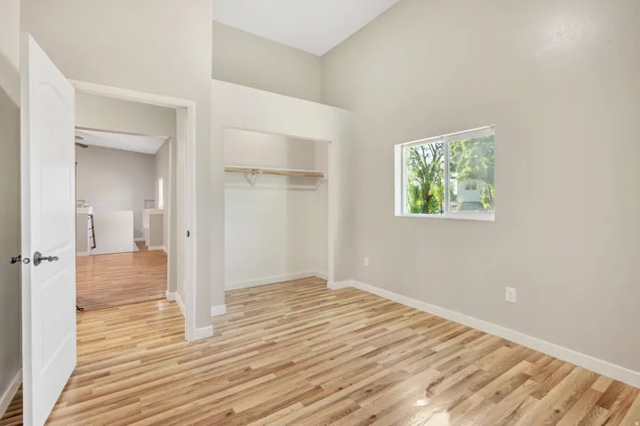 Bedroom featuring wood-finish flooring, a double-hung window, a built-in closet with shelving and hanging rod, a contemporary white door, and vaulted ceilings