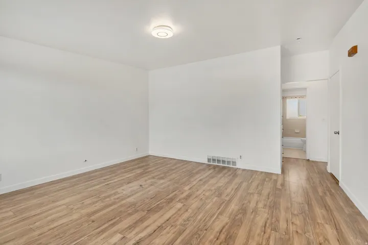 Spacious interior room with wood-finish flooring, white walls, and a contemporary flush-mount ceiling light