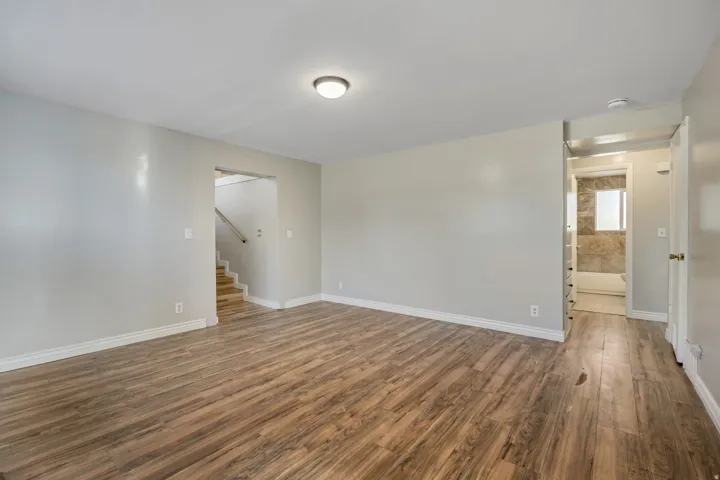 Spacious room featuring wood-finish flooring, light grey painted walls, white baseboards, and a flush-mount ceiling light