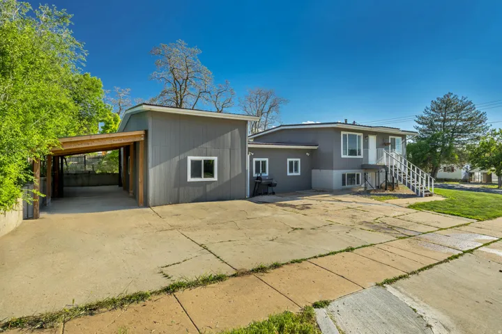 Property exterior featuring a carport with wood beam construction, a split-level residence with gray siding, white window trim, and a concrete driveway