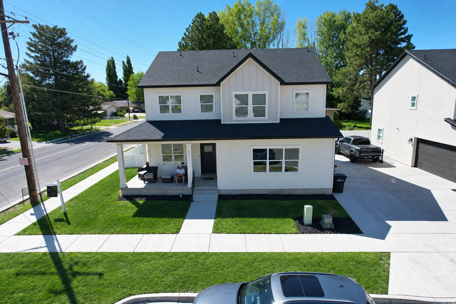 Two-story white exterior with black trim, covered front porch, concrete walkway, attached two-car garage, and a manicured lawn