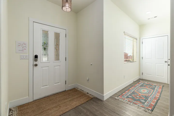 Entryway featuring a white paneled front door with decorative glass inserts, wood-finish flooring, a contemporary ceiling light fixture, and a secondary white paneled door