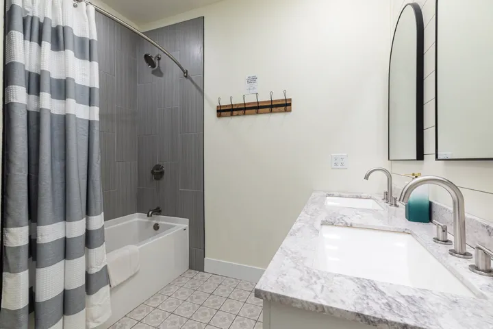 Primary EnSuite Bathroom featuring a dual vanity with undermount sinks and a patterned countertop, individual arched mirrors, and a tub-shower combination with vertical tile surround
