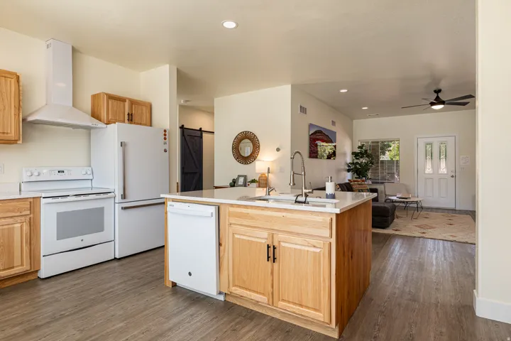Kitchen featuring a central island with a sink and light wood cabinetry, white appliances, and wood-finish flooring