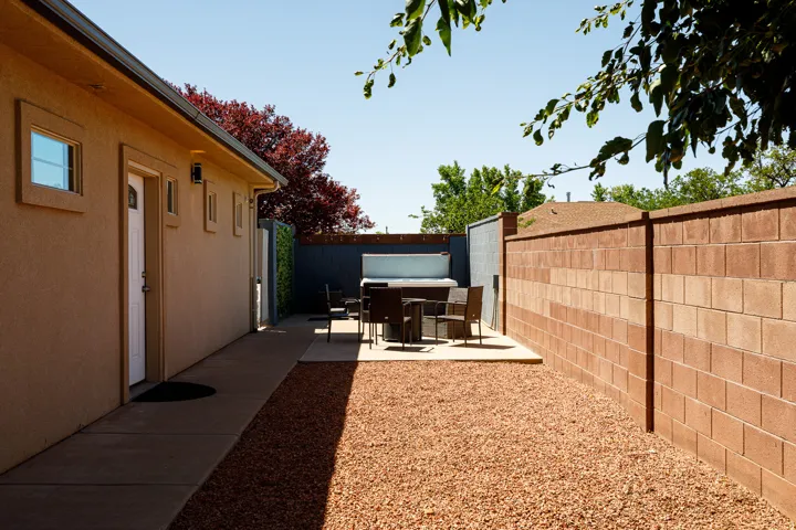 Exterior stucco siding with a concrete walkway, rock landscaping, block privacy wall, and an outdoor patio area