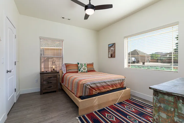 Bedroom featuring wood-finish flooring, a ceiling fan with integrated lighting, and a large window with blinds