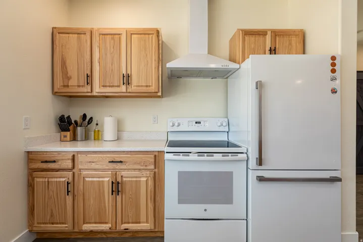 Kitchen featuring wood cabinetry, light-colored countertops, a white electric range, and a white refrigerator