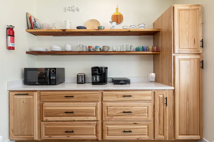 Light wood-finish cabinetry with black hardware, white speckled countertop, and two floating wood-finish shelves