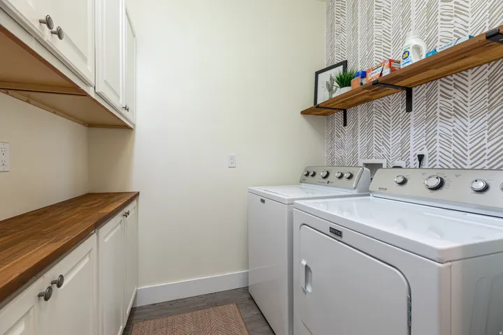 Laundry area featuring wood-finish countertops, white shaker cabinetry with dark hardware, and a patterned accent wall