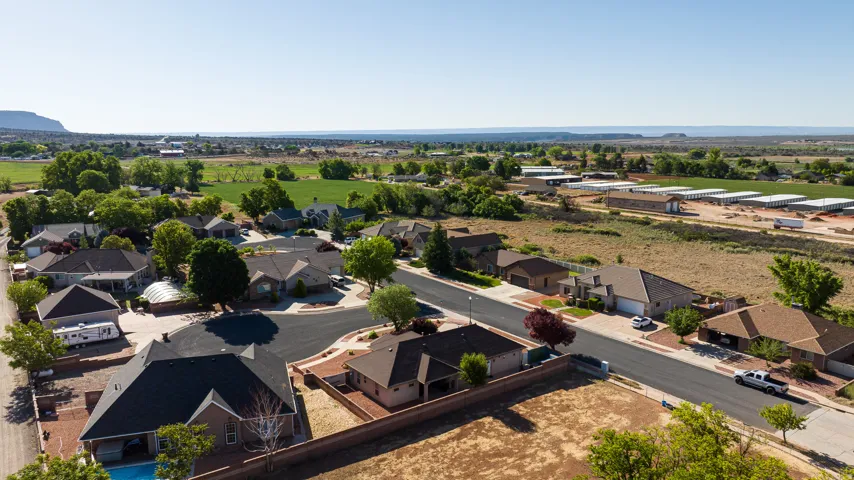 Residential neighborhood with paved streets and established homes, bordered by agricultural fields and distant hills