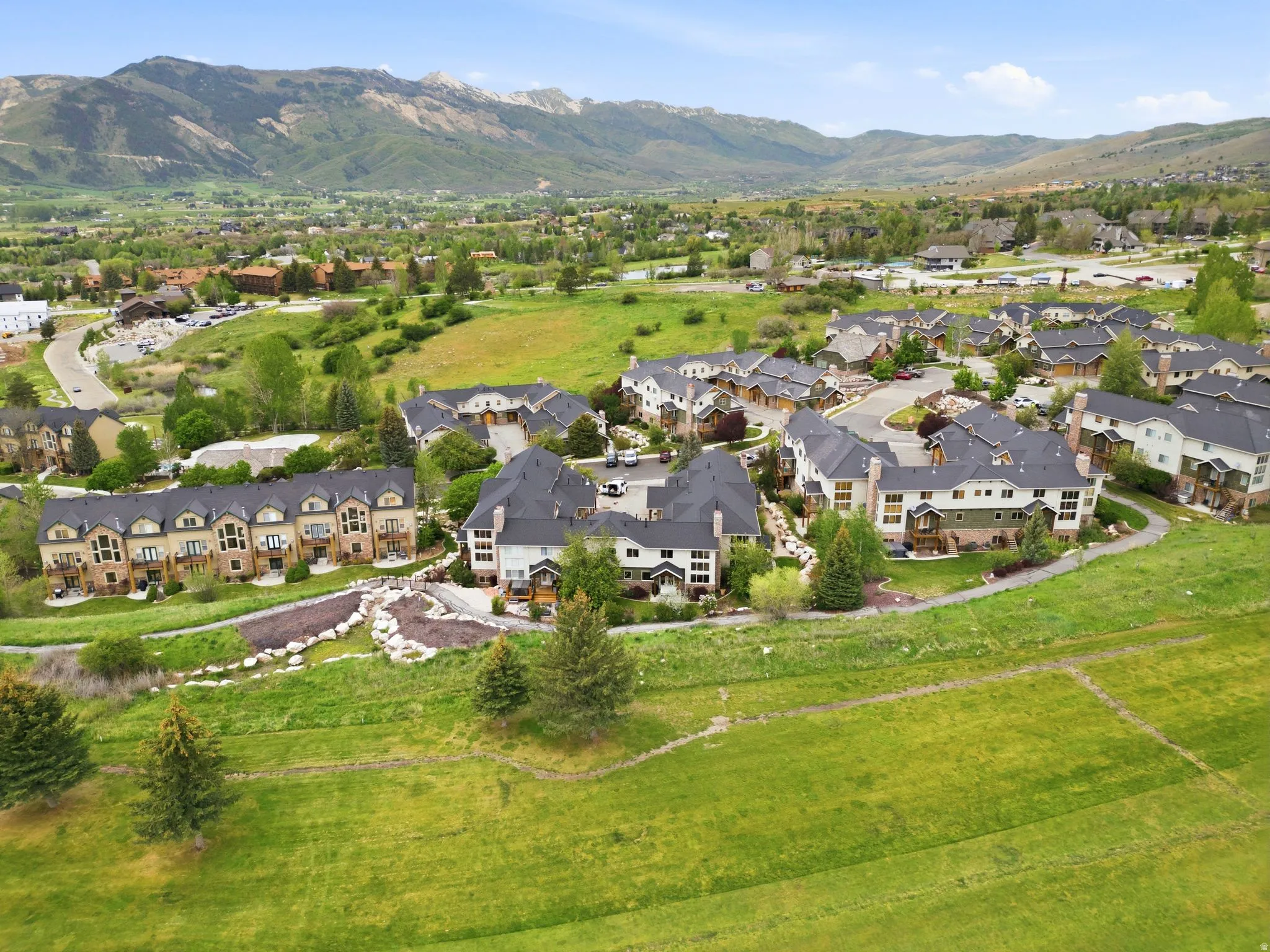 Expansive hillside community featuring multiple multi-story townhome-style residences with dark roofing, light-toned siding, and surrounding green spaces