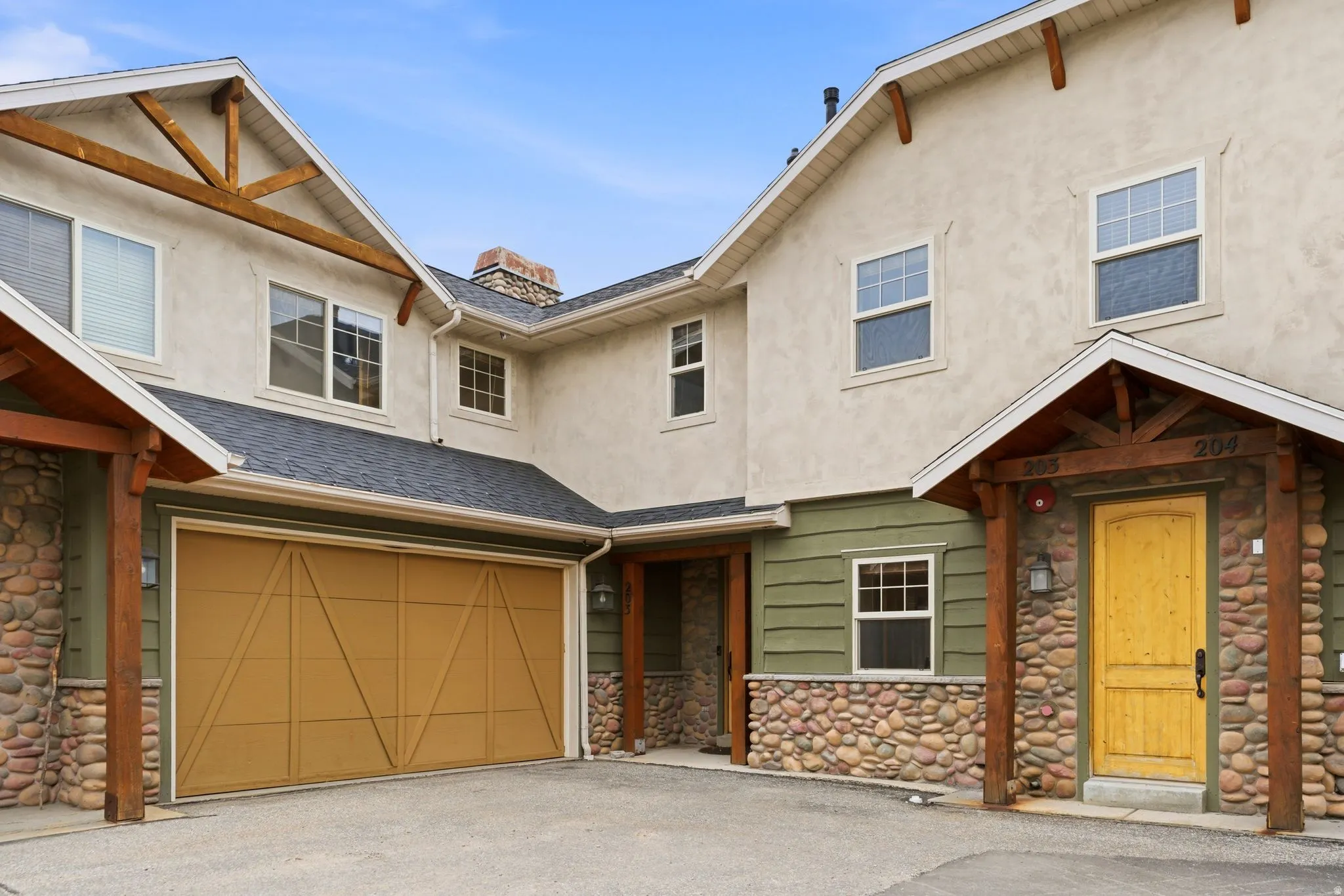 Exterior featuring stucco and river stone accents, a prominent garage with a wood-finish door, and a covered entry with a distinctive yellow front door
