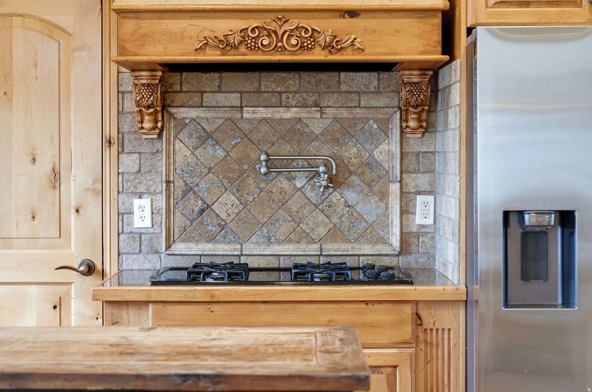 Built-in gas cooktop with a decorative tile backsplash and a wall-mounted pot filler