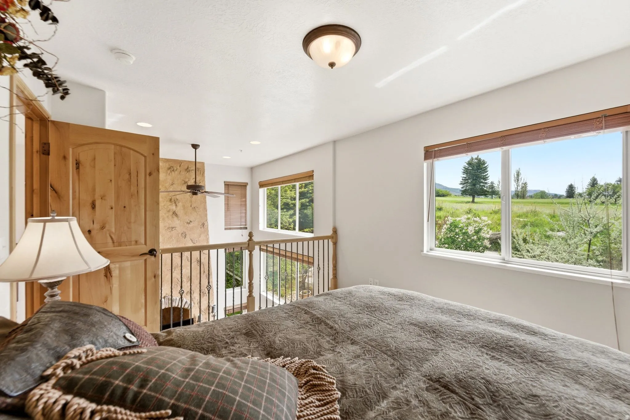 Loft space featuring a natural wood panel door, iron baluster railing, and ceiling fan
