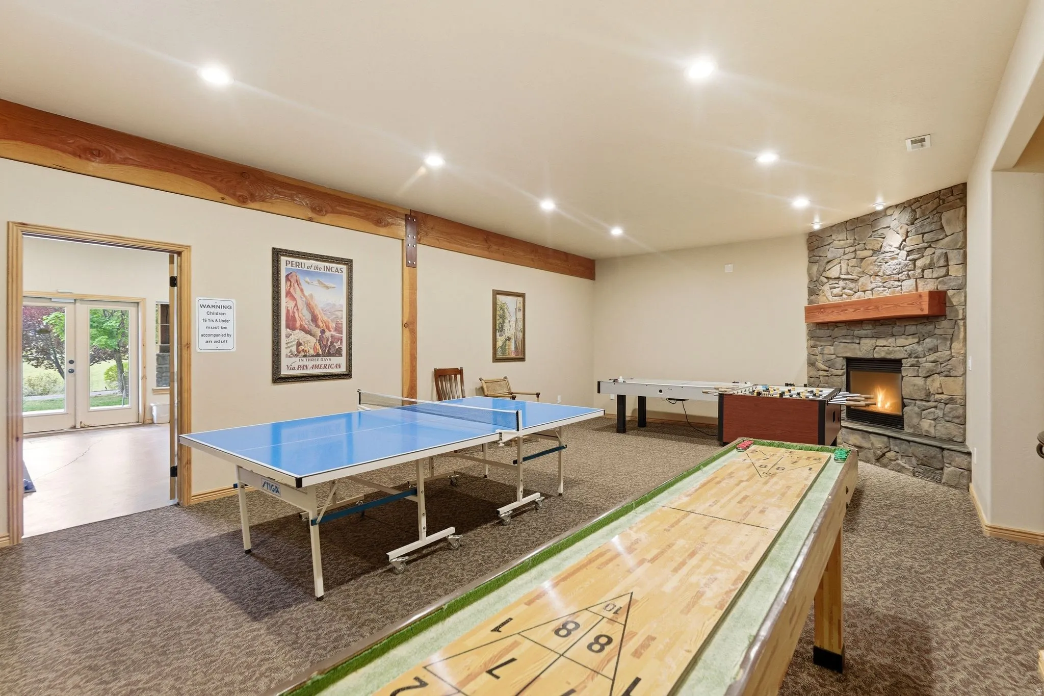 Spacious recreation room featuring recessed lighting, exposed wood beams, and a stone-clad fireplace with a wood mantel