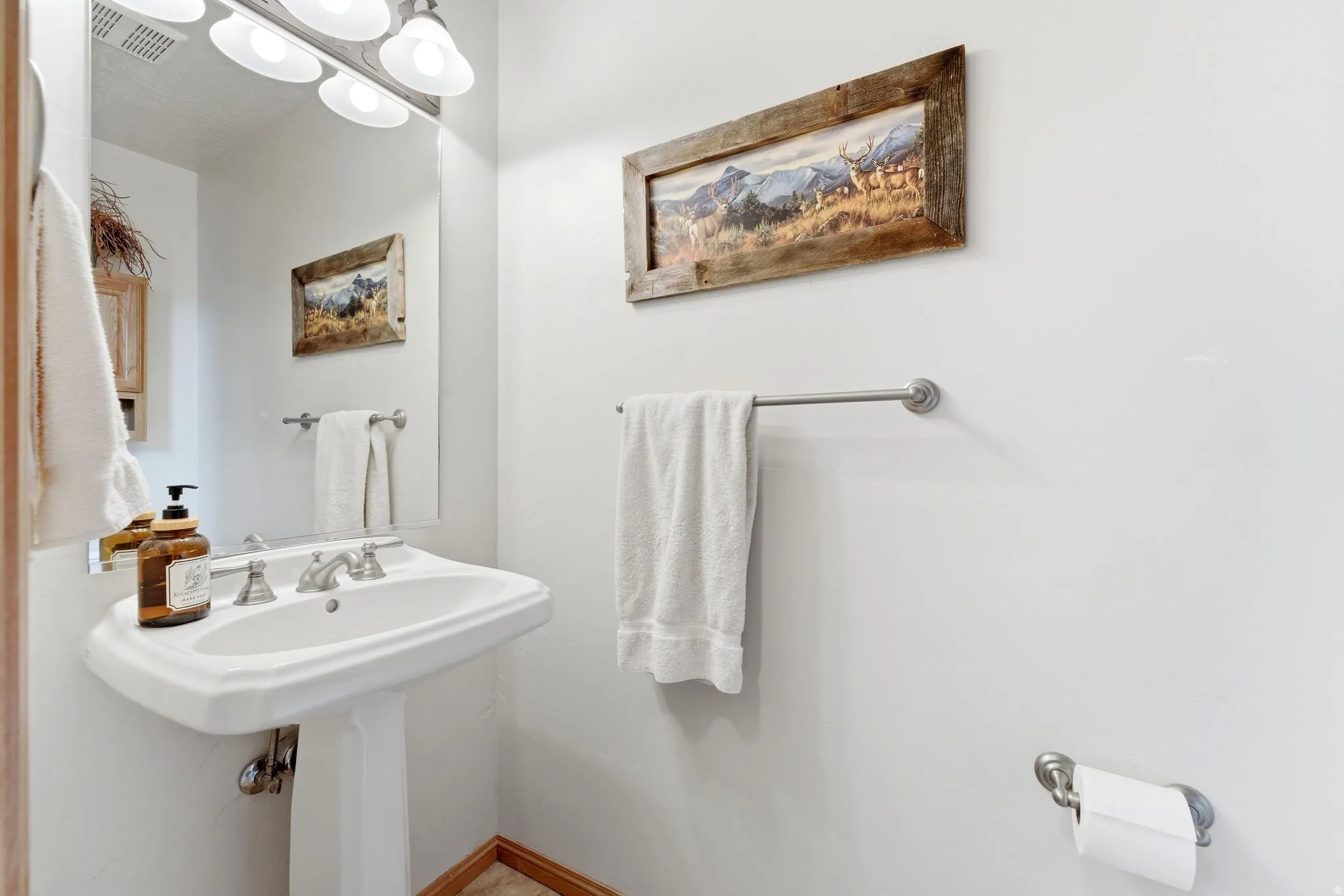 White pedestal sink with a dual-handle faucet, illuminated by a four-light vanity fixture