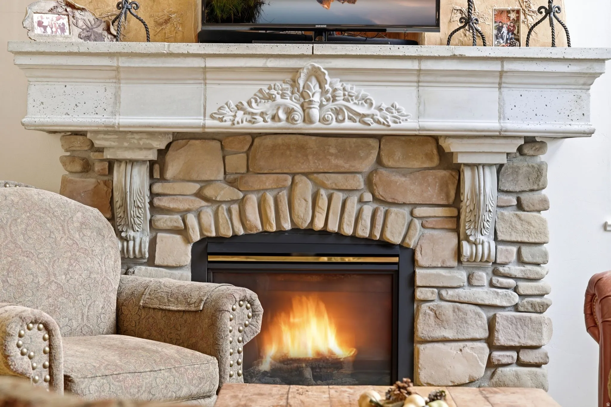 Stone fireplace with an arched firebox and a decorative cast stone mantelpiece featuring corbels and carved detailing