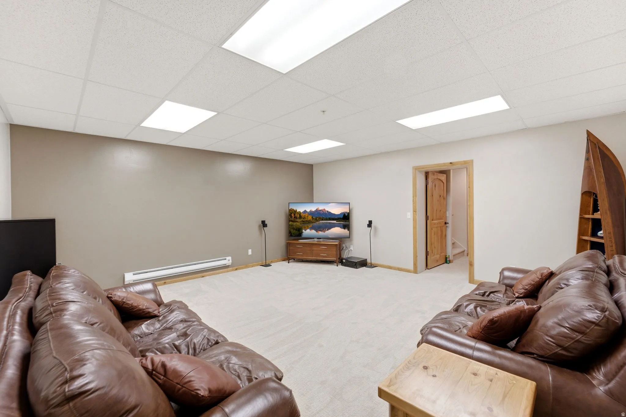 Spacious recreational room featuring light-colored carpeting, a drop ceiling with integrated lighting, and neutral wall tones