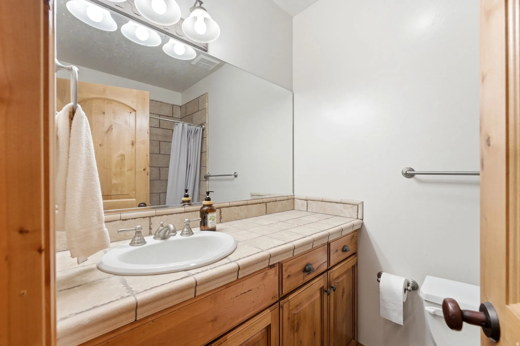 Bathroom vanity featuring a tiled countertop, undermount sink, and wood-finish cabinetry