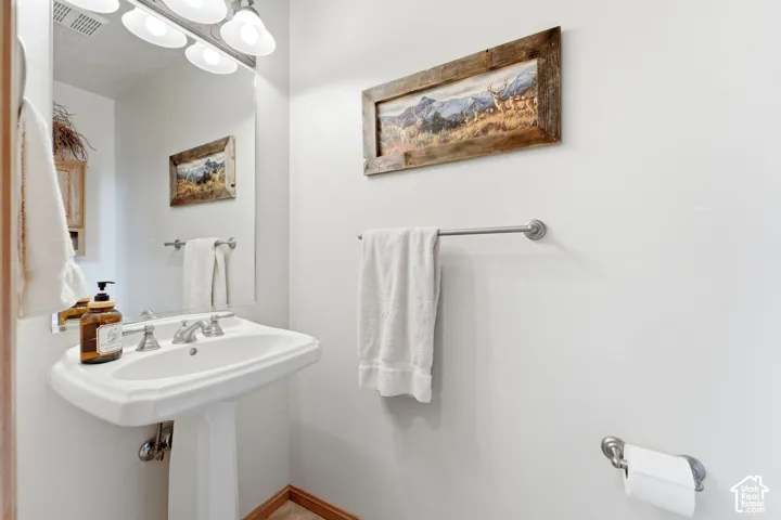 White pedestal sink with a dual-handle faucet, illuminated by a four-light vanity fixture