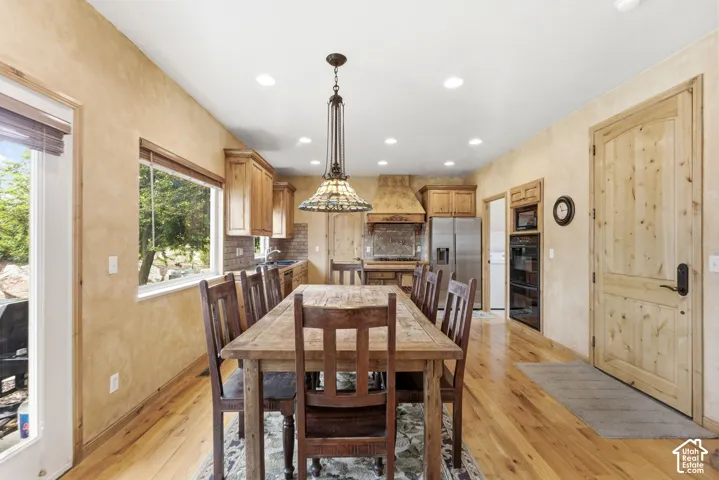 Spacious kitchen and dining area featuring wood-finish flooring, recessed lighting, wood cabinetry, a tile backsplash, and stainless steel appliances