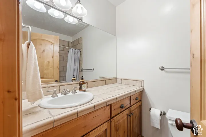 Bathroom vanity featuring a tiled countertop, undermount sink, and wood-finish cabinetry