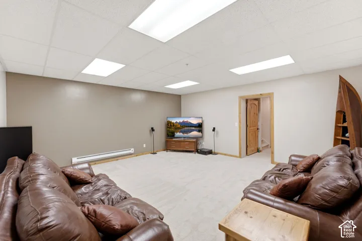 Spacious recreational room featuring light-colored carpeting, a drop ceiling with integrated lighting, and neutral wall tones