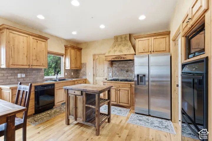 Kitchen featuring light wood cabinetry, a decorative range hood, stainless steel side-by-side refrigerator, and hardwood flooring
