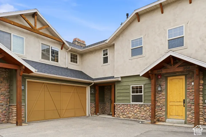 Exterior featuring stucco and river stone accents, a prominent garage with a wood-finish door, and a covered entry with a distinctive yellow front door
