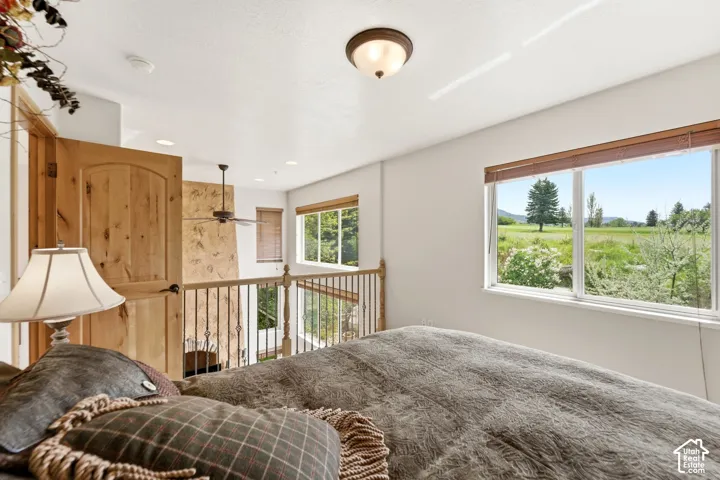 Loft space featuring a natural wood panel door, iron baluster railing, and ceiling fan