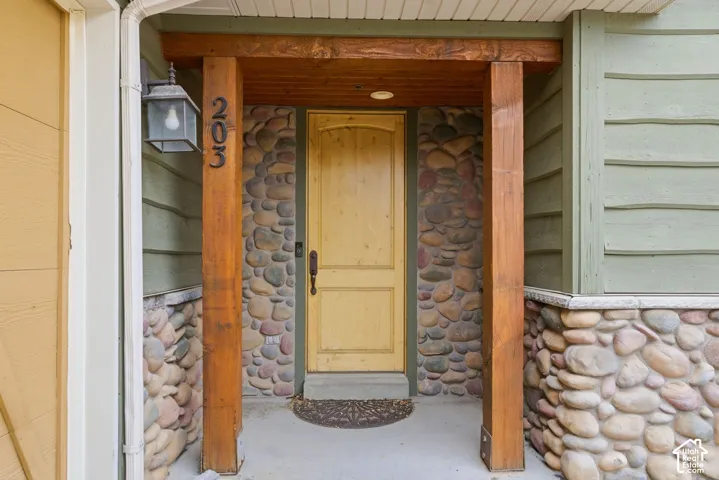 Entryway featuring a natural wood door, stacked stone facade, exposed wood beams, and a concrete porch
