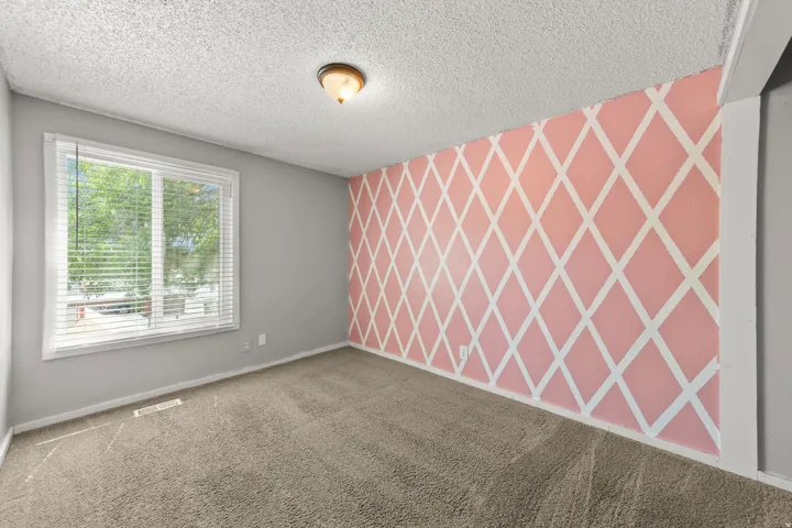 Wall-to-wall carpeting, window with blinds, decorative accent wall, neutral wall paint, and ceiling-mounted light fixture