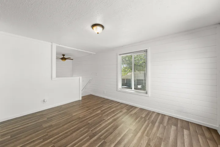 Wood-finish flooring with white shiplap walls and a double-hung window with blinds