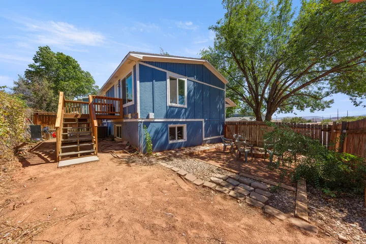 Split-level exterior with blue siding, a wooden deck, and a fenced yard with mature trees
