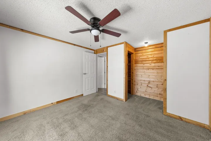 Textured ceiling with a ceiling fan, light gray carpet, and wood paneling accents